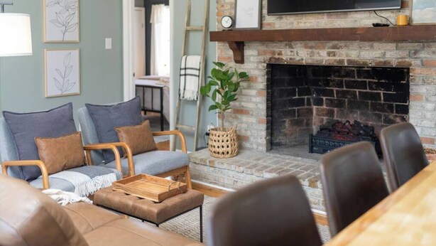 Un salon chaleureux avec une cheminée en briques, un téléviseur à écran plat fixé au-dessus, et un coin repas avec une table et des chaises en bois.