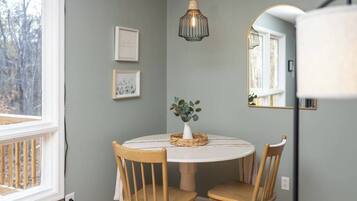 Un comedor con una mesa redonda, dos sillas de madera, un florero con hojas verdes y una lámpara colgante.