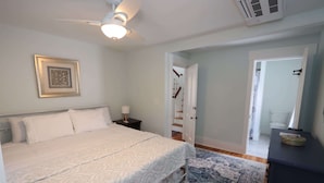 A bedroom with a bed, a nightstand, a ceiling fan, a framed picture, a door leading to a bathroom, and a small table with a decorative item. - Downtown Ogunquit Single home, 3 Bedroom (Ogunquit)