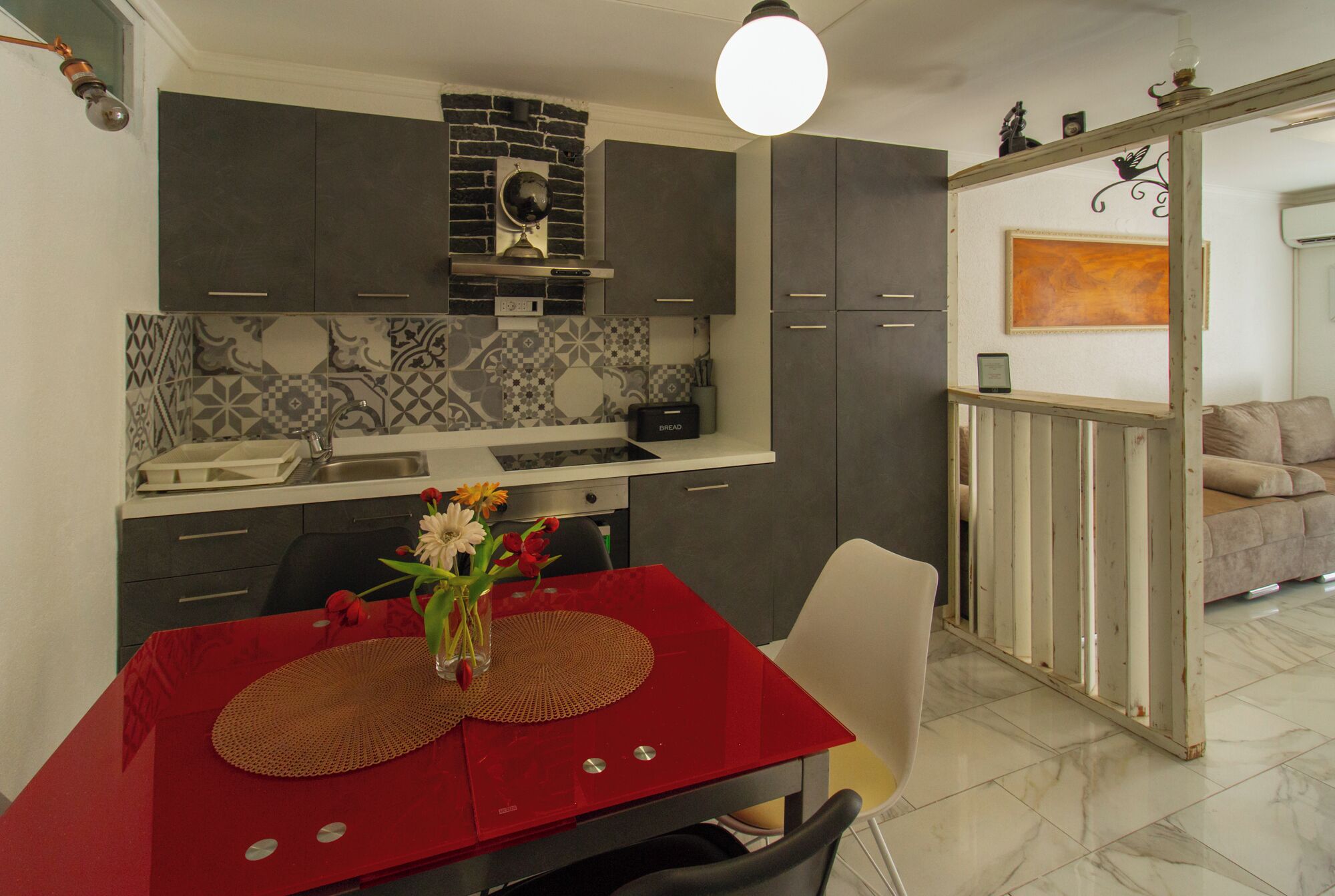 A modern kitchen with dark cabinets, a red dining table, and a vase of flowers.