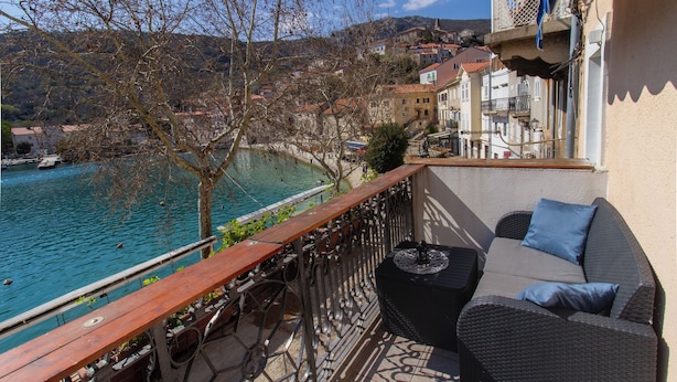 Ein Balkon mit Korbmöbeln, Blick auf eine Küstenstadt und ein Gewässer.