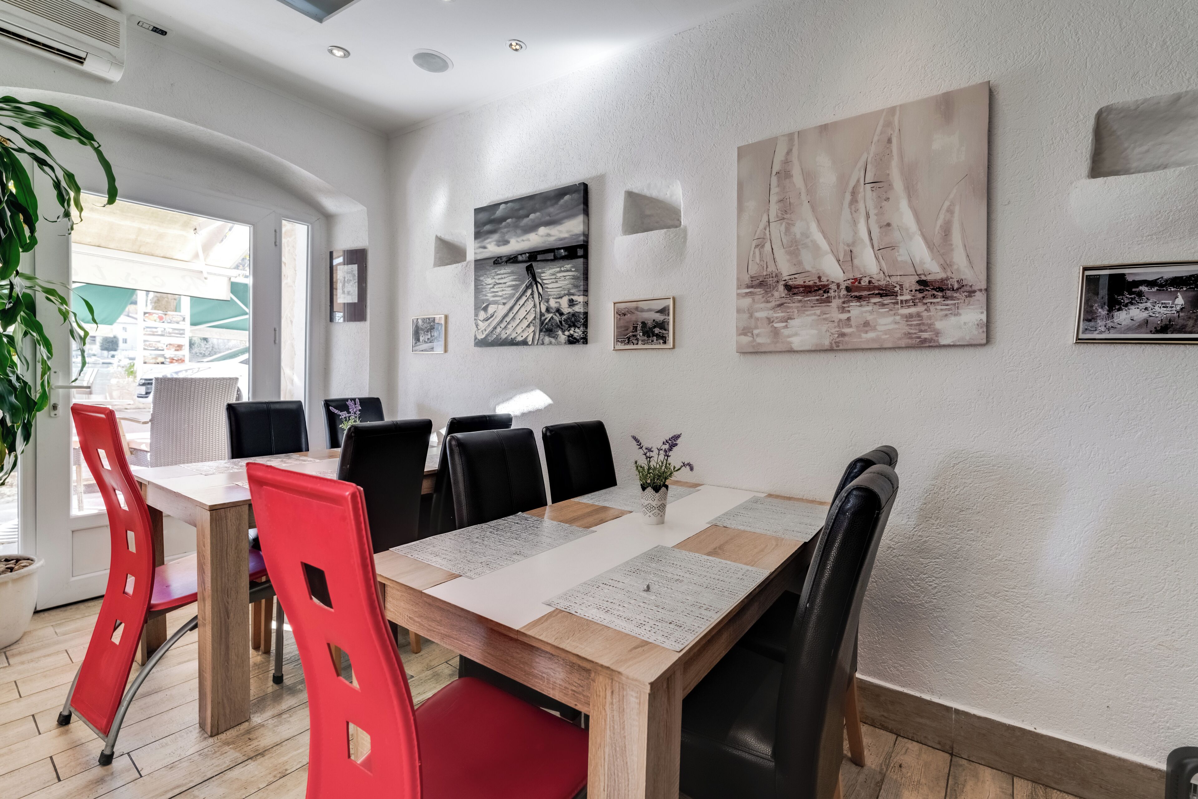 Zona pranzo con tavolo in legno, sedie nere e rosse e opere d'arte alle pareti.