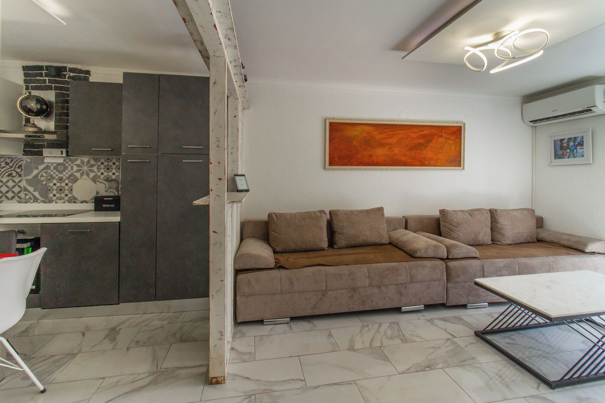 Una sala de estar moderna con un sofá, una mesa de centro y una cocina con armarios y salpicadero de azulejos.