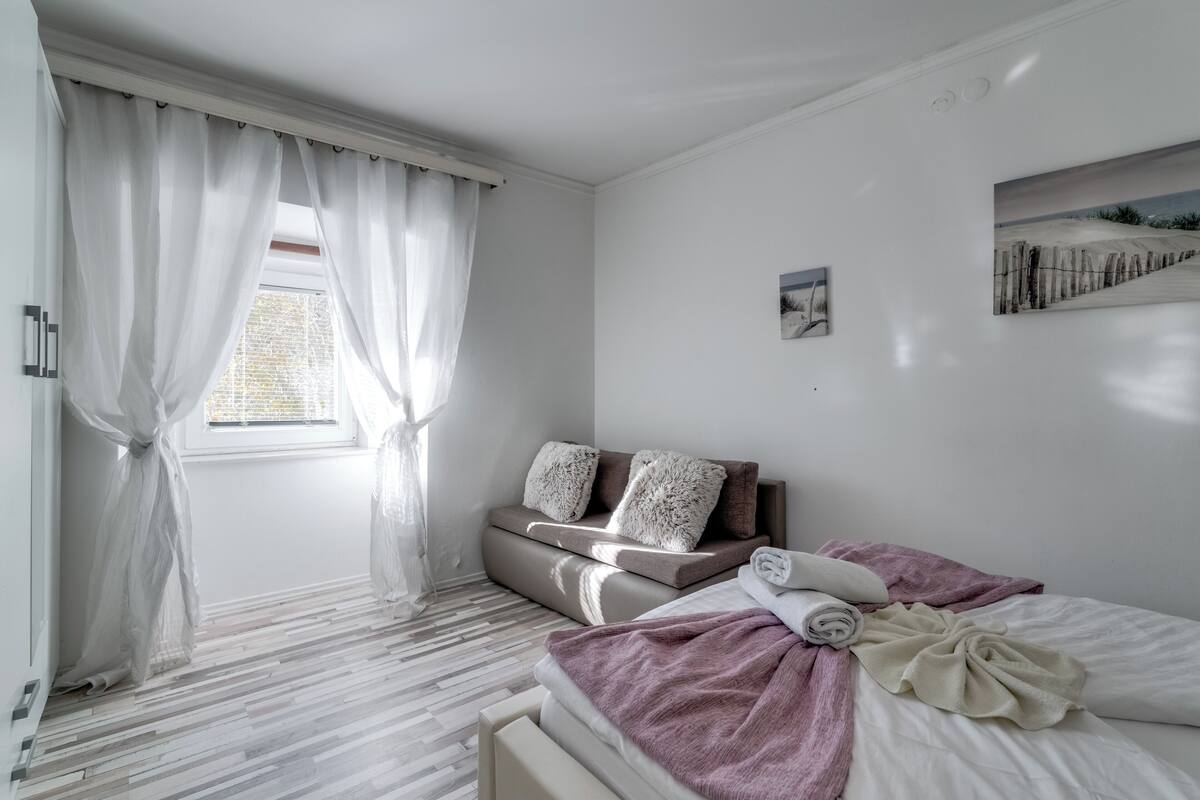 A bedroom with a bed, a sofa, and a window with curtains.