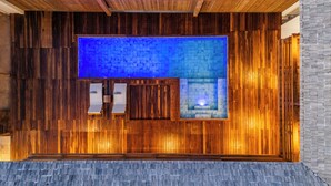 Un mur en bois, une piscine dont le fond est recouvert de carreaux bleus, deux chaises longues blanches et un mur en pierre.