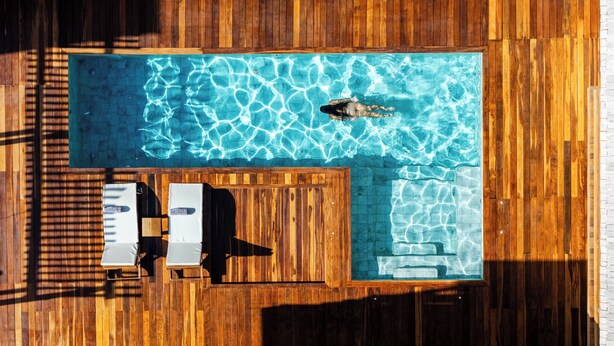 Vue aérienne d’une piscine avec une terrasse en bois, deux chaises longues et une clôture en bois.
