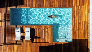 An aerial view of a swimming pool with wooden deck, two sun loungers, and a wooden fence.