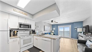 A modern kitchen with white appliances, a dining area with a blue wall, and a balcony with a view. - Seacrest 905 by Liquid Life (Gulf Shores)