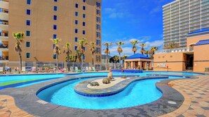 A swimming pool with a fountain, palm trees, and a building with balconies. - Crystal Tower 807 by Liquid Life (Gulf Shores)