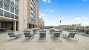 A poolside area with lounge chairs, a swimming pool, and a tall building in the background.