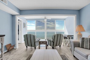 Una habitación con vista al océano, dos sillones a rayas, una mesa de centro blanca y una lámpara.