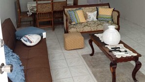 Ein Wohnzimmer mit einem braunen Sofa, einem gemusterten Sofa, einem Holztisch und einem Essbereich mit Tisch und Stühlen.