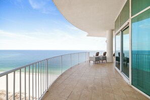 Un balcon avec vue sur l’océan, une table avec des chaises et une porte vitrée.