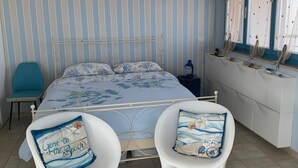 Un dormitori amb un llit, dues cadires blanques, una petita taula de nit i una finestra amb cortines.