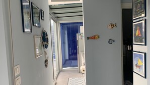 Un passadís amb sòl de rajola, una porta que dona a un bany i una vista d'una altra habitació amb cortina blava.