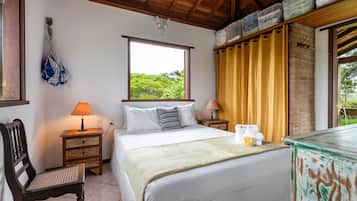 A neatly arranged bedroom with a large bed, a wooden chair, two bedside tables with lamps, a window with a view of greenery, and a brick wall.