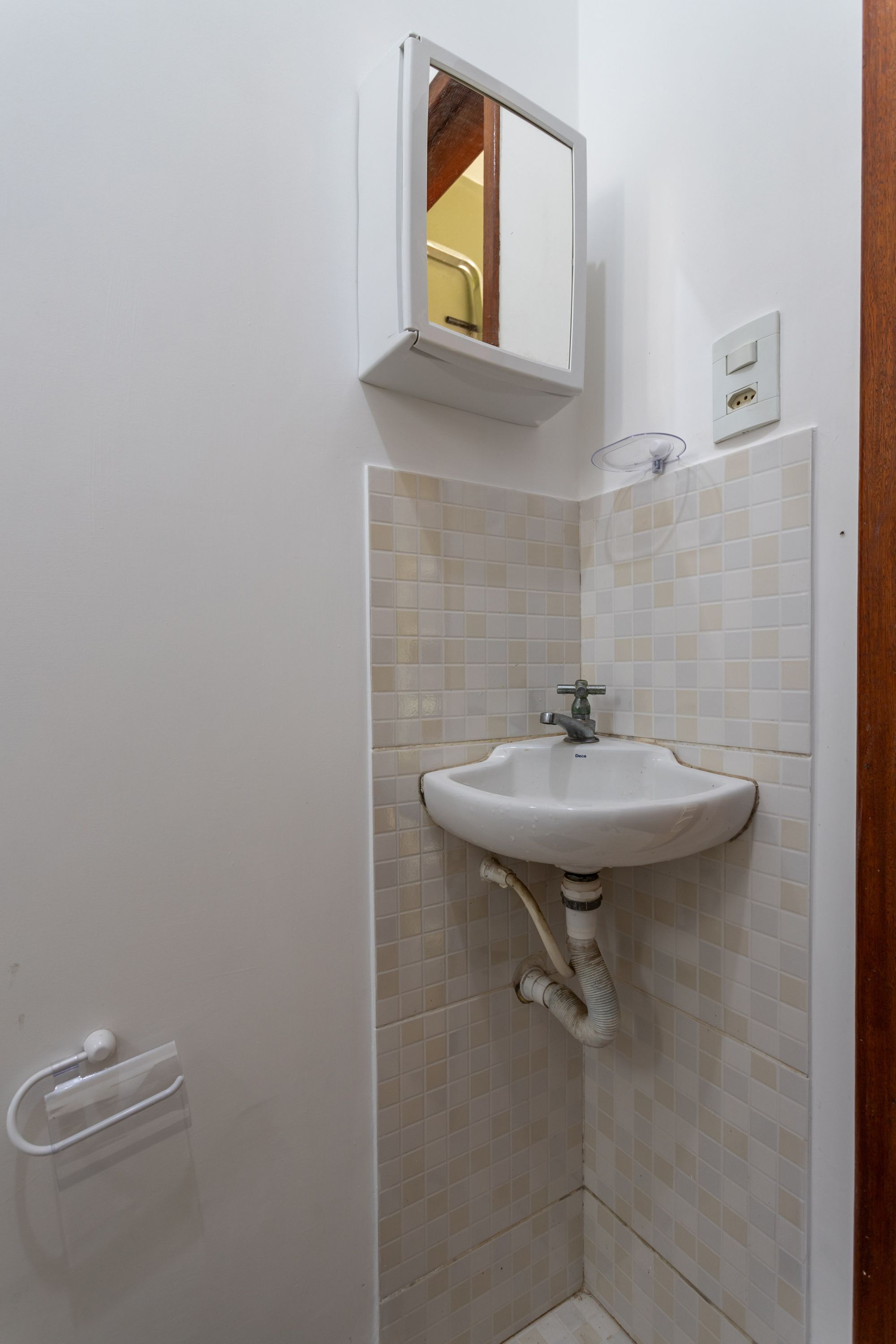 Un baño pequeño con un lavamanos blanco, un espejo encima y una pared con azulejos.