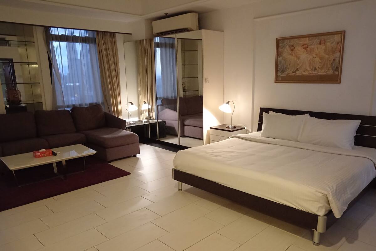 A hotel room with a bed, a sofa, a coffee table, a desk, and a chair.