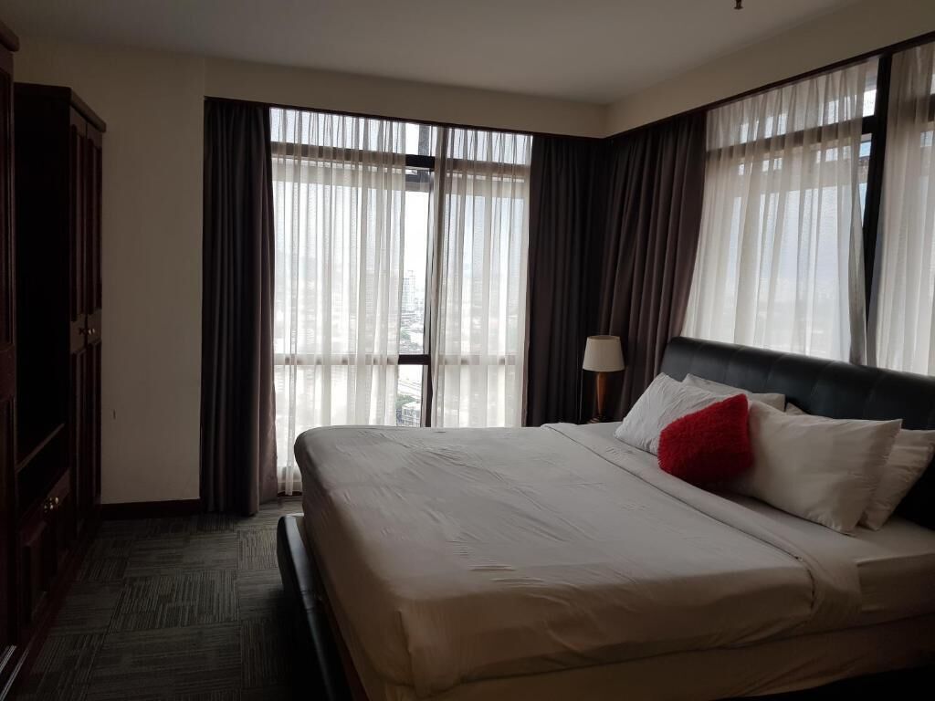 Een hotelkamer met een groot bed, een bureau en uitzicht op de stad door dunne gordijnen.