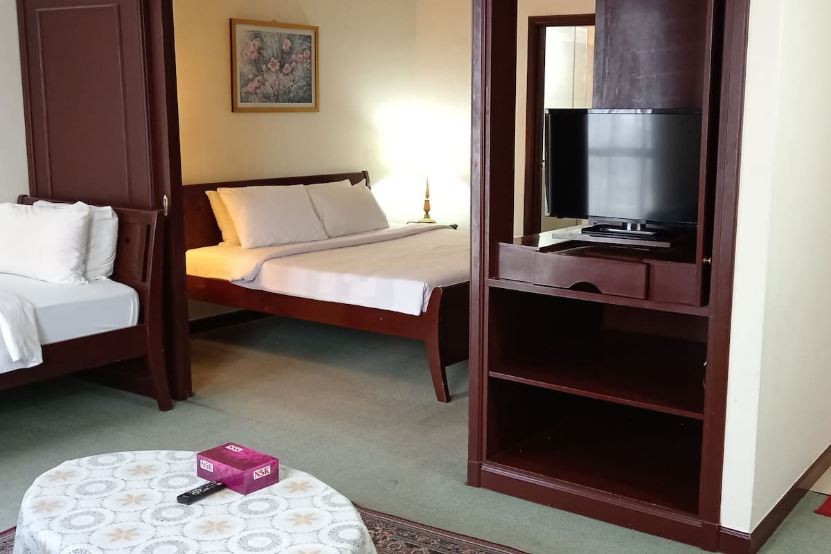A hotel room with a bed, a TV, a small table with a remote control, and a bathroom visible through an open door.