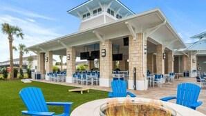 An outdoor patio area with blue Adirondack chairs, a fire pit, and a covered seating area with tables and chairs.