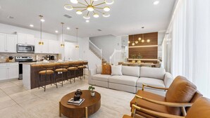 A modern kitchen with white cabinets, a stainless steel microwave, and a bar area with stools.
