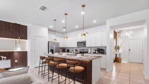 A modern kitchen with white cabinets, a central island with bar stools, stainless steel appliances, and pendant lighting.