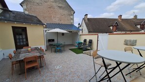 A patio area with a table and chairs, a covered seating area, and a view of a building in the background. - Gîte de l'olivier, reception room, parties and ceremonies, events. (Saint-Brisson-sur-Loire)