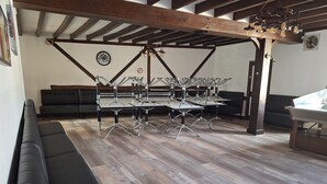 A modern interior with a dining area featuring metal tables and chairs, a black sofa, and a wooden ceiling structure. - Gîte de l'olivier, reception room, parties and ceremonies, events. (Saint-Brisson-sur-Loire)