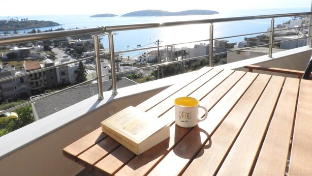 A balcony with a wooden table, a book, and a coffee mug. - Elea Sea View Apartment in Ag. Nikolaos (Agios Nikolaos)