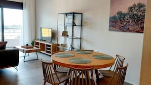 A modern dining area with a round wooden table, six chairs, and a glass cabinet with a painting. - Elea Sea View Apartment in Ag. Nikolaos (Agios Nikolaos)