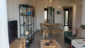 A modern living room with a wooden coffee table, a TV, a bookshelf, and a dining area with chairs and a table. - Elea Sea View Apartment in Ag. Nikolaos (Agios Nikolaos)