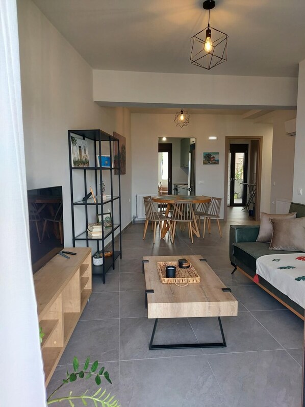 A modern living room with a wooden coffee table, a TV, a bookshelf, and a dining area with chairs and a table.