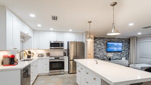 A modern kitchen with white cabinetry, stainless steel appliances, a large island, and a stone backsplash.