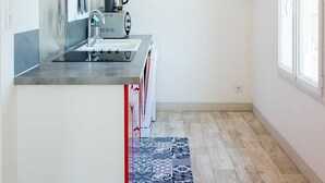 Une cuisine moderne avec des meubles blancs, un mur d’accent rouge, une cuisinière intégrée et une fenêtre laissant entrer la lumière naturelle.