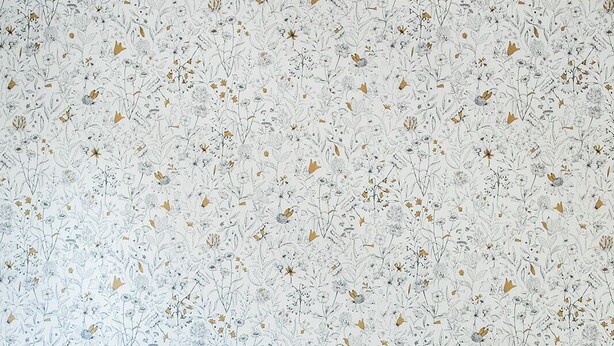 Un lit avec deux oreillers de couleur moutarde et une tête de lit en osier, le tout placé devant un mur orné d’un motif floral.