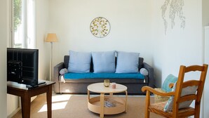 Un salon avec un canapé gris, une table basse ronde en bois, une chaise en bois, un téléviseur posé sur un bureau et une carte du monde accrochée au mur.