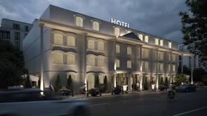 Un hôtel à la façade classique, doté de grandes fenêtres et d’une enseigne « HÔTEL » bien visible.