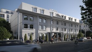 Un grand hôtel à plusieurs étages, de style architectural classique, avec une entrée imposante, un porche couvert et une enseigne indiquant « HÔTEL ».
