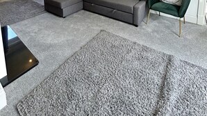 Ein modernes Wohnzimmer mit einem grauen Ecksofa, einem grünen Sessel und einem kleinen Tisch.