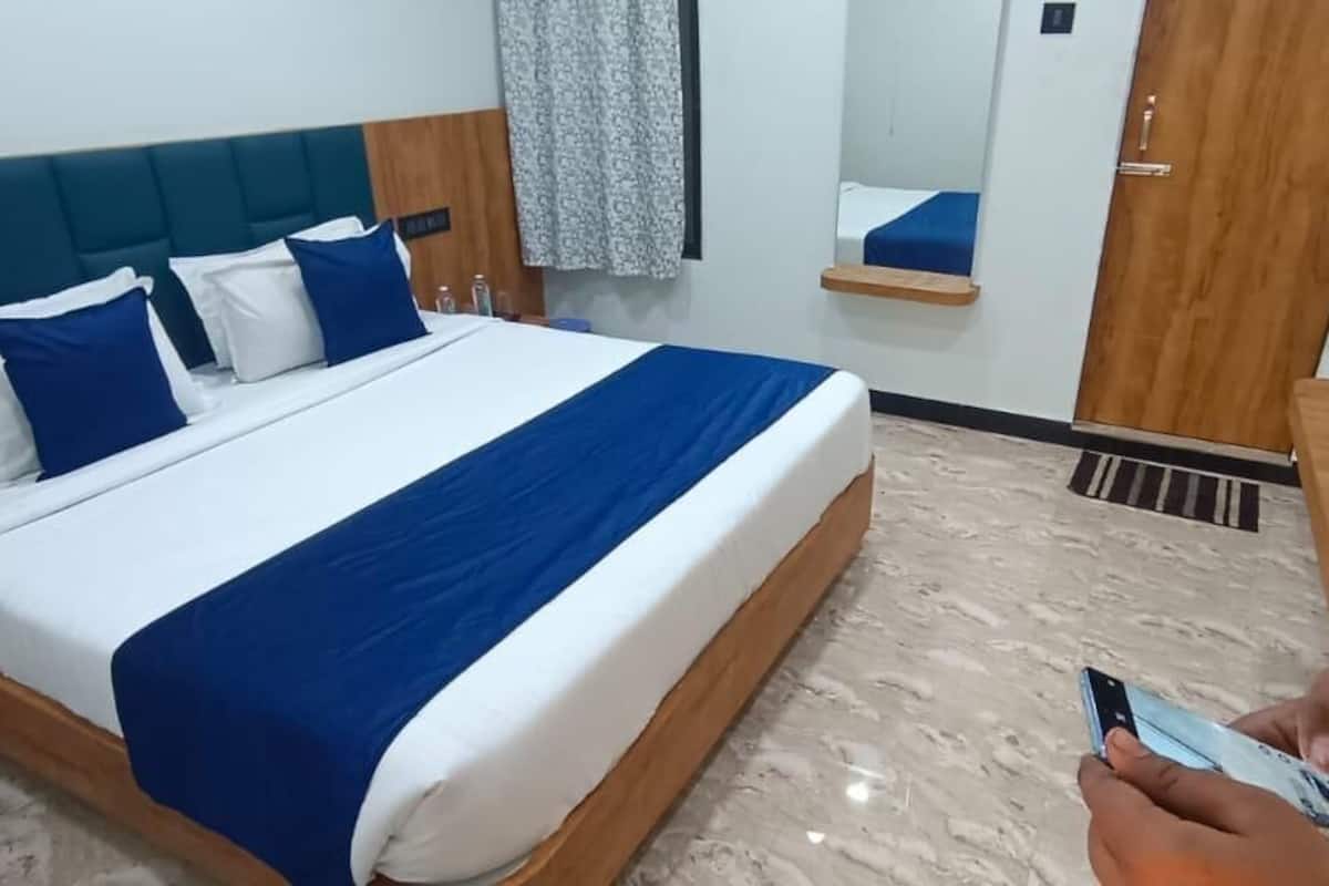 A hotel room with a bed, a wooden nightstand, a mirror, and a bathroom door.