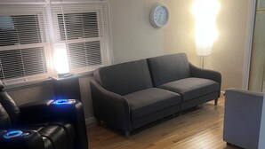 A living room with a dark grey sofa, a massage chair with blue lights, a wooden floor, and a wall clock. - Charming 1-bedroom house with WiFi, AC in enchanting Burnsville (Burnsville)