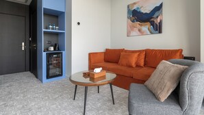 A modern living room with a blue shelving unit, a glass coffee table, an orange sofa, and a grey armchair.
