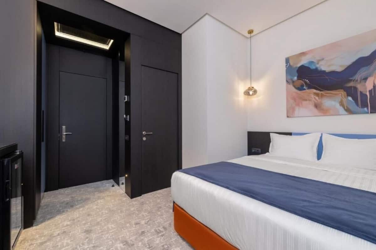 Moderni hotellihuone, jossa on suuri sänky, tumma puinen vaatekaappi ja taulu seinällä.