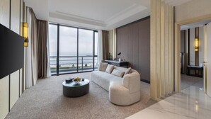 A modern hotel room with a large window, a sofa, a coffee table, and a flat-screen TV.