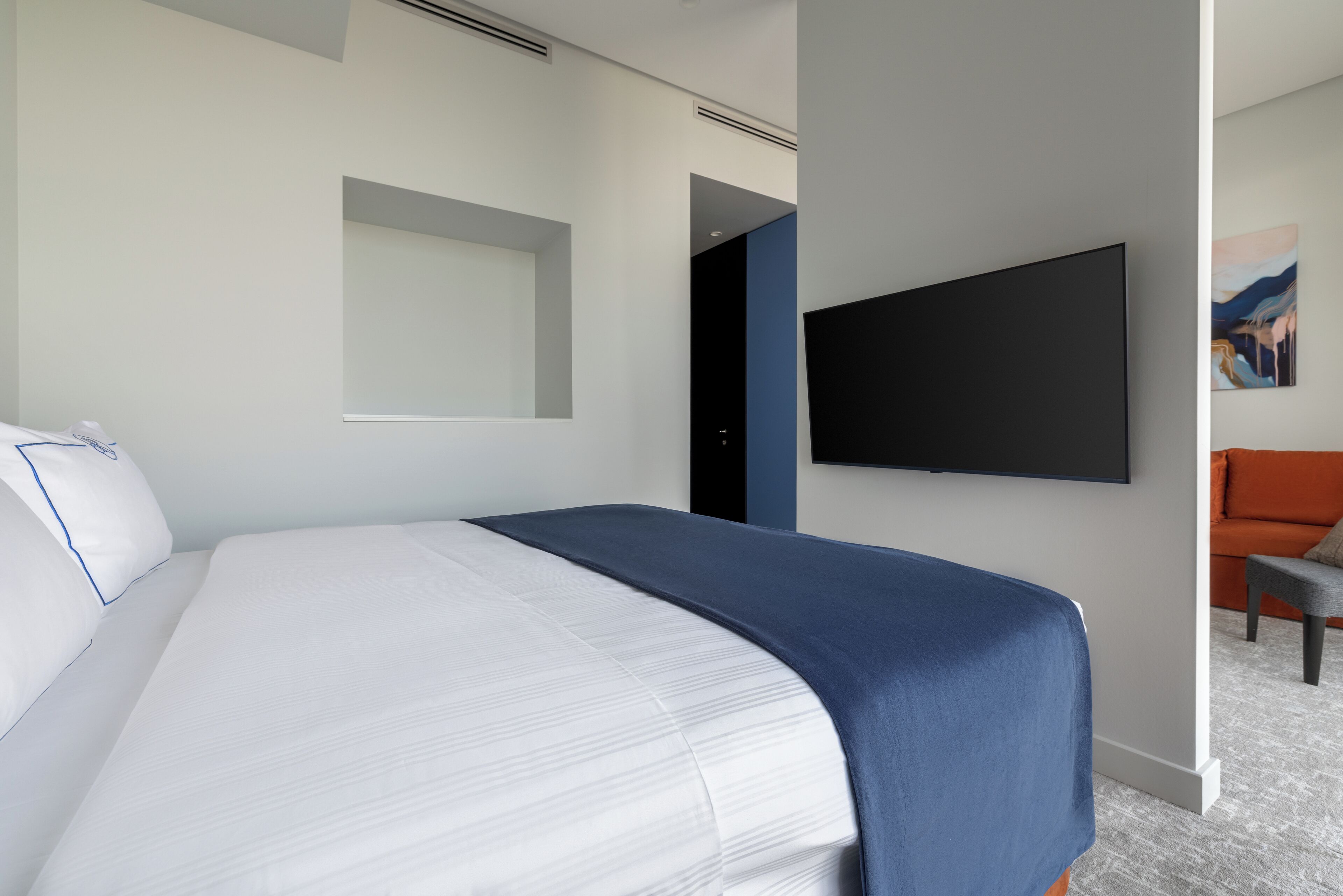 Una habitación de hotel moderna con una cama grande, un televisor de pantalla plana montado en la pared y un rincón de estar con sofá y sillón.