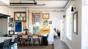 A dining area with a long table and chairs, a kitchen area with a hanging pot rack, and a hallway leading to a bedroom. - Historic Rooftop Steps to DT Shops & Dining Unit 5 (Tuscaloosa)