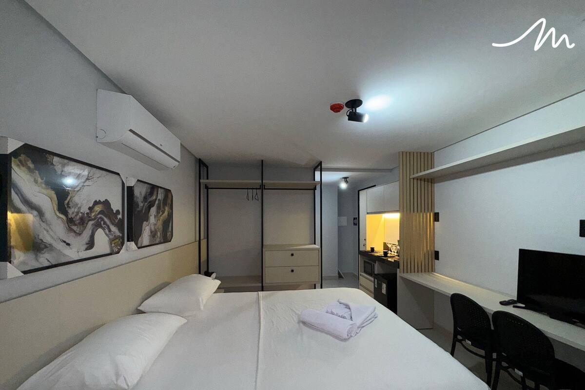 A hotel room with a bed, a desk, a chair, a TV, and artwork on the wall.