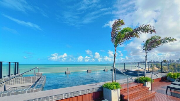A pool area with a view of the ocean and a city skyline. - Alta Garden (João Pessoa)