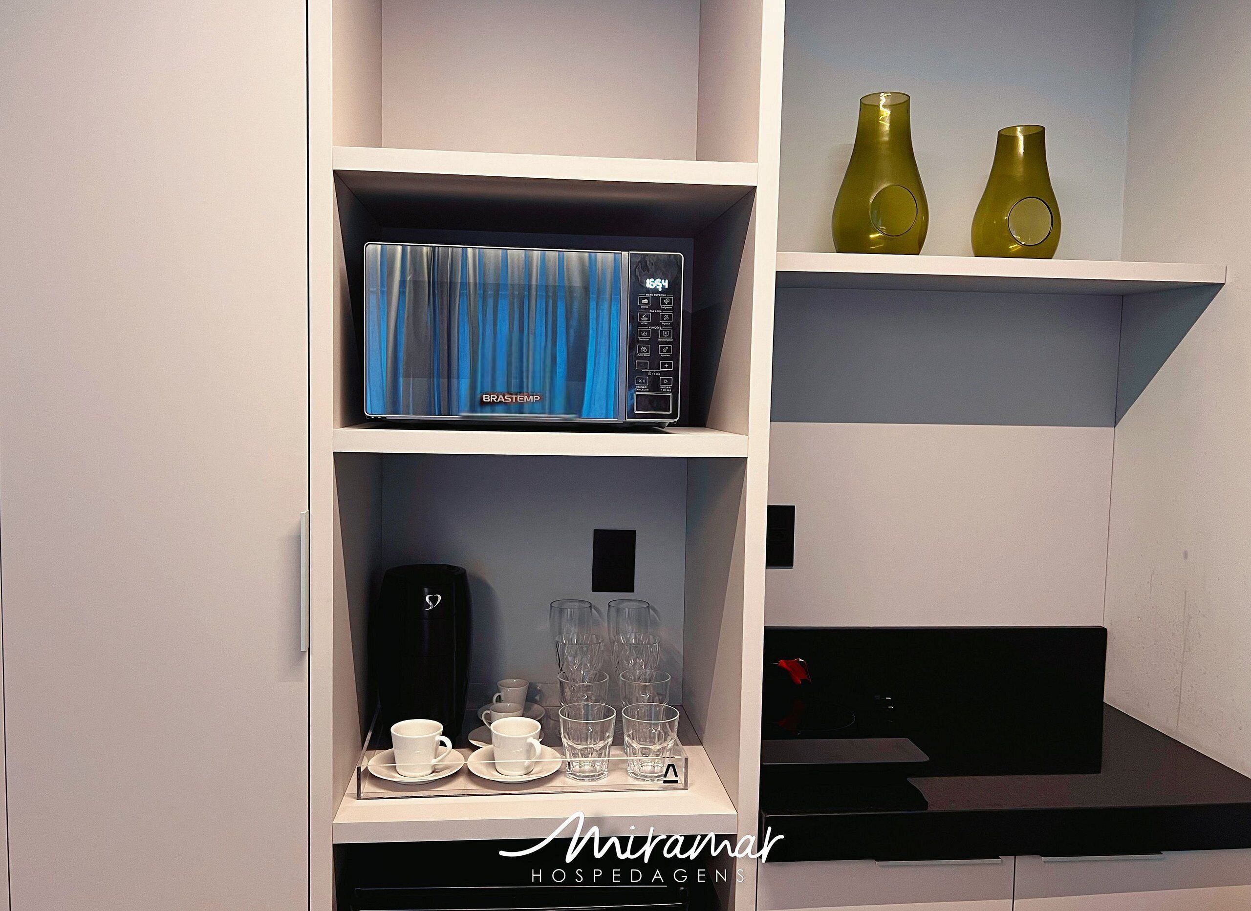 Una cocina con cafetera, cristalería y microondas en los estantes.